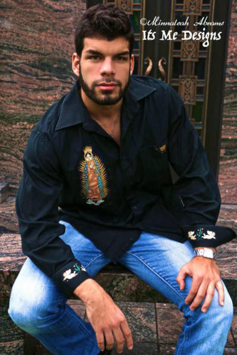 May include: A man wearing a black long-sleeved button-down shirt with a colorful embroidered image of the Virgin Mary. The shirt has white embroidered details on the cuffs. He is wearing blue jeans and a silver watch.