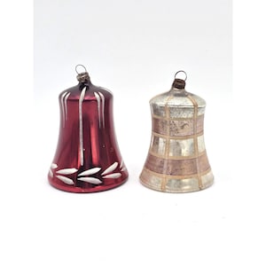 May include: Two vintage glass bell ornaments. One is a deep red with white accents and the other is silver and tan with a grid pattern. Both have metal loops for hanging and are likely for a Christmas tree.