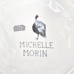May include: White ceramic plate featuring a speckled bird design. The plate includes the text "MADE IN CHINA", "FABRIQU&Eacute; EN CHINE", "DISHWASHER SAFE", "MICROWAVE SAFE", and "MICHELLE MORIN".