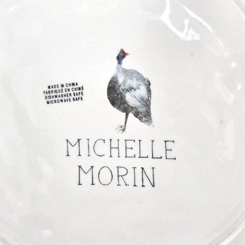 May include: White ceramic plate featuring a speckled bird design. The plate includes the text "MADE IN CHINA", "FABRIQU&Eacute; EN CHINE", "DISHWASHER SAFE", "MICROWAVE SAFE", and "MICHELLE MORIN".