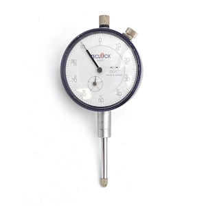 May include: A precision dial indicator with a white face, black numerals, and a black bezel. The dial reads from 0 to 100, with a smaller dial at the bottom. The indicator has a silver stem and is labeled "TECLOCK A1921".