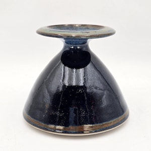 May include: A dark blue ceramic pedestal bowl with a flared base and a wide, flat rim. The bowl has a glossy finish with a brown and green rim. The bowl is likely used for serving or display.