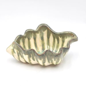 May include: A ceramic bowl with a leaf-like shape. The bowl features a wavy rim and is painted with a cream base and green vertical stripes. The rim has a dark brown edge. The bowl is approximately 8 inches long.