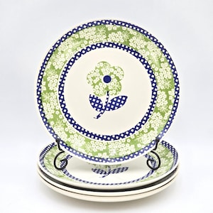 May include: A set of ceramic plates with a floral design. The plates feature a white base with a green floral border and a blue checkered pattern. The center of each plate has a flower design with a blue checkered stem and a green flower.