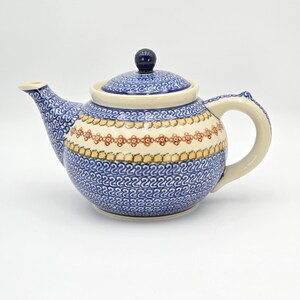 May include: A ceramic teapot with a blue and white floral pattern. The teapot has a cream-colored handle and spout, and a dark blue knob on the lid. The design includes a band of orange and yellow floral accents.
