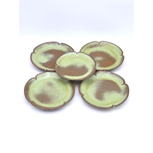 May include: Five ceramic plates with a scalloped edge. The plates have a light green and brown color scheme. The plates are arranged in a circular pattern against a white background.