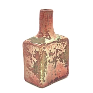May include: A square-shaped, vintage ceramic vase with a narrow neck. The vase has a textured surface with a mottled appearance in shades of red, brown, and green. The vase is likely used for decorative purposes.