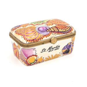 May include: A rectangular trinket box with a hinged lid. The box is cream-colored with a colorful seashell design and the words "St. Martin West Indies." The box has gold-colored metal trim and a clasp.