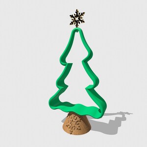Pode incluir: Um cortador de biscoitos de árvore de Natal de plástico verde com um floco de neve dourado no topo. O cortador está sentado em uma base marrom.