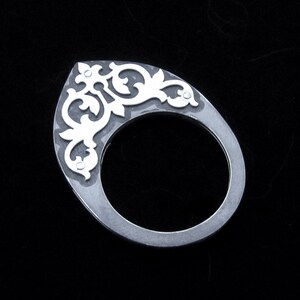 May include: A silver ring with a decorative filigree design. The ring is made of metal and has a smooth, polished finish.