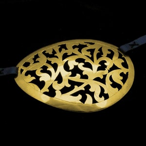 May include: A gold-coloured eye patch with a decorative, intricate floral design. The eye patch is made of metal and has a delicate, filigree pattern.
