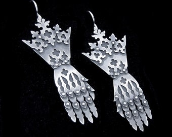 Puede incluir: Un par de pendientes de plata con forma de manos con diseños intrincados. Los pendientes están hechos de metal y tienen un aspecto delicado y ornamentado.