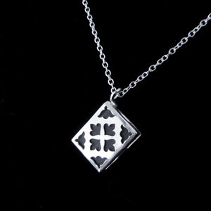 May include: A silver necklace with a pendant featuring a geometric design with a black background. The pendant is shaped like a square with rounded corners and has a cutout design.