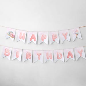 Op de afbeelding: Een roze en witte banner met de woorden "Happy Birthday" gespeld in roze letters versierd met donuts en ijshoorns.