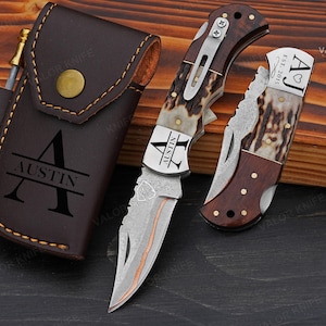 May include: A brown leather knife case with the name "AUSTIN" and a large letter "A" is next to two folding knives. The knives have wooden handles and silver blades. One knife has the name "AUSTIN" on the blade. The other knife has the initials "AJ" and the year "2015".