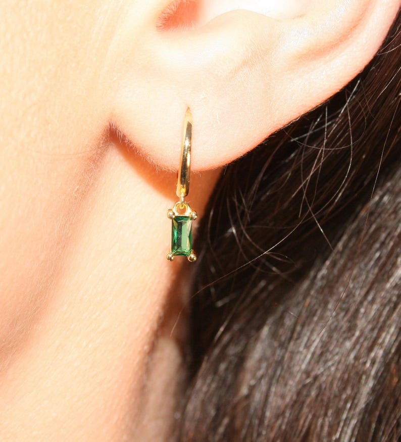 K&ouml;nnte beinhalten: Goldene Creolen mit einem baumelnden rechteckigen Smaragd-Edelstein.