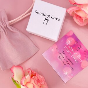 K&ouml;nnte beinhalten: Eine rosa und wei&szlig;e Geschenkbox mit dem Text "Sending Love" und einer kleinen Schleife. Eine rosa und wei&szlig;e Karte mit dem Text "Sparkle This Christmas" und "Have a sparkly Christmas and a Happy New Year".