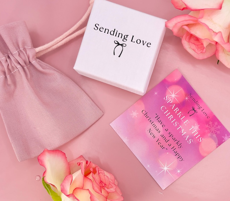 K&ouml;nnte beinhalten: Eine rosa und wei&szlig;e Geschenkbox mit dem Text "Sending Love" und einer kleinen Schleife. Eine rosa und wei&szlig;e Karte mit dem Text "Sparkle This Christmas" und "Have a sparkly Christmas and a Happy New Year".