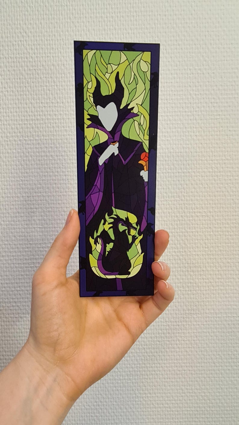 Puede incluir: Un marcap&aacute;ginas de estilo vitral con una silueta de Mal&eacute;fica de La Bella Durmiente de Disney. El marcap&aacute;ginas es morado, verde y amarillo con una silueta negra de Mal&eacute;fica y su drag&oacute;n.
