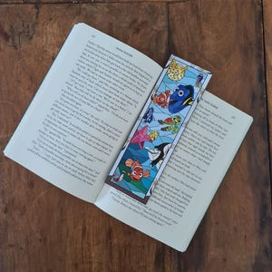 Può includere: Un segnalibro colorato con personaggi del film d'animazione Alla ricerca di Nemo. Il segnalibro è fatto di vetro e presenta un design a vetri colorati. I personaggi includono Marlin, Dory, Nemo e Crush. Il segnalibro è perfetto per ogni fan del film.