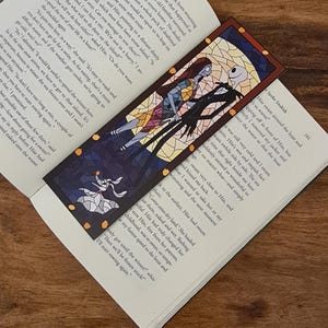 Può includere: Un segnalibro in vetro colorato con Jack Skellington e Sally del film L'Incubo prima di Natale. Il segnalibro è un rettangolo lungo con una cornice nera e un design in vetro colorato. I personaggi sono raffigurati in una posa romantica, con Jack che tiene la mano di Sally. Lo sfondo è blu scuro con stelle e una luna crescente. Il segnalibro è perfetto per ogni fan del film.