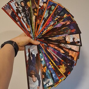 Può includere: Un set di 18 segnalibri colorati con diversi personaggi dell'Universo Cinematografico Marvel. Ogni segnalibro è realizzato con un design a vetri colorati con un bordo nero.