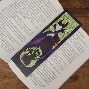 Puede incluir: Un marcap&aacute;ginas de vitral con Mal&eacute;fica de La Bella Durmiente de Disney. El marcap&aacute;ginas es morado, verde y negro con una imagen detallada de Mal&eacute;fica con su ic&oacute;nico vestido morado y su tocado con cuernos. El texto "Spoke Snakish" es visible en la esquina inferior derecha del marcap&aacute;ginas.