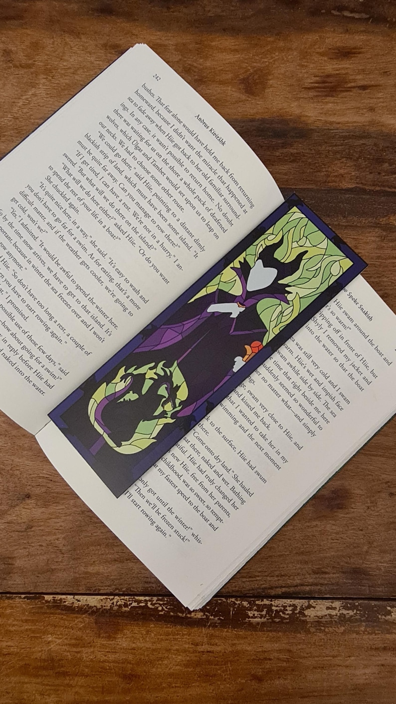 Puede incluir: Un marcap&aacute;ginas de vitral con Mal&eacute;fica de La Bella Durmiente de Disney. El marcap&aacute;ginas es morado, verde y negro con una imagen detallada de Mal&eacute;fica con su ic&oacute;nico vestido morado y su tocado con cuernos. El texto "Spoke Snakish" es visible en la esquina inferior derecha del marcap&aacute;ginas.