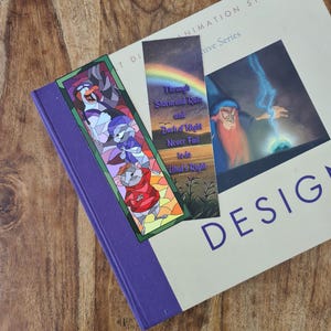 Op de afbeelding: Twee kleurrijke bladwijzers met illustraties in de stijl van glas-in-lood. De eerste bladwijzer toont een muis, een pingu&iuml;n en een kat. De tweede bladwijzer toont een tovenaar met een regenboog en de tekst "Through Storm and Rain and Dark of Night Never Fail to do What's Right".