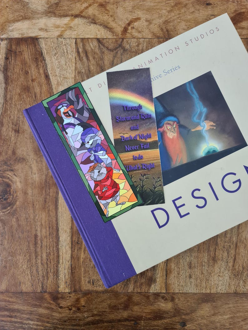 Op de afbeelding: Twee kleurrijke bladwijzers met illustraties in de stijl van glas-in-lood. De eerste bladwijzer toont een muis, een pingu&iuml;n en een kat. De tweede bladwijzer toont een tovenaar met een regenboog en de tekst "Through Storm and Rain and Dark of Night Never Fail to do What's Right".