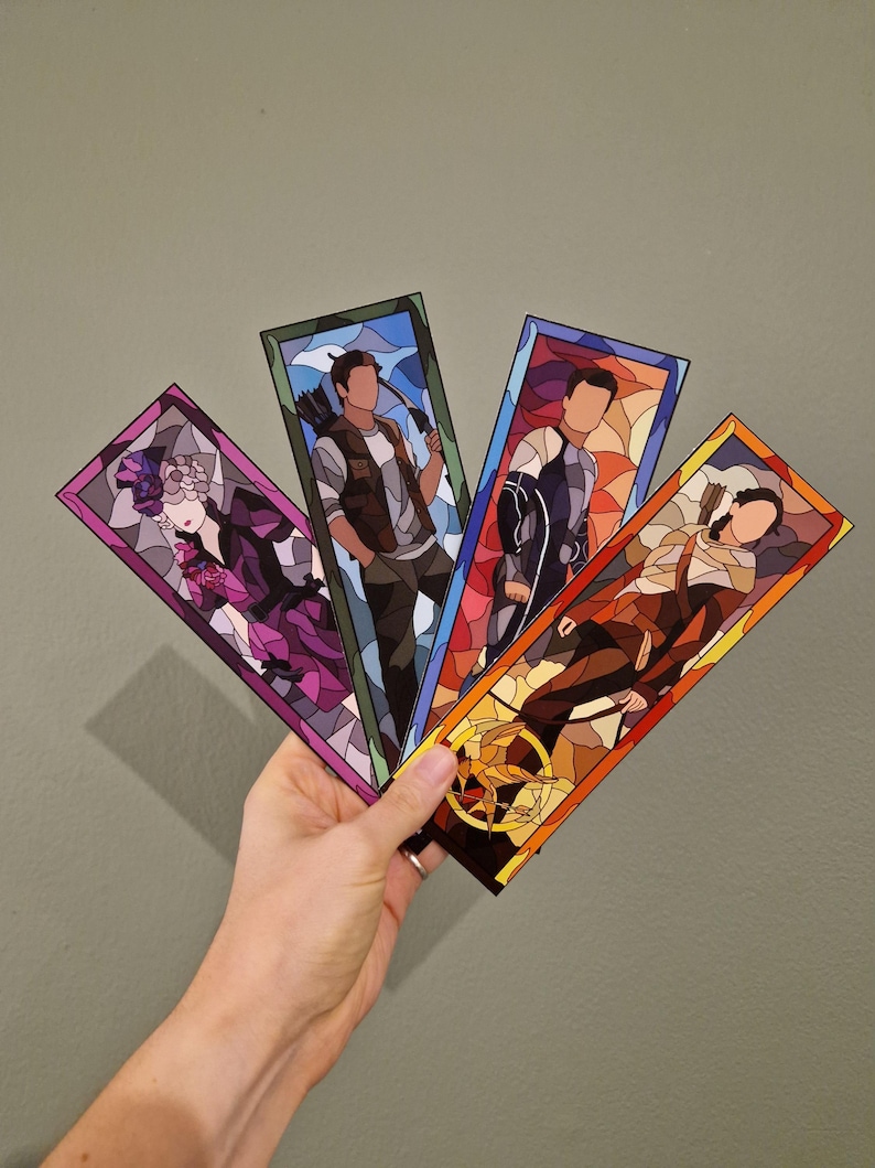 May include: Four rectangular bookmarks with stained glass style illustrations. Each bookmark features a different character, with vibrant colors and detailed designs. The bookmarks are held in a hand against a neutral background.