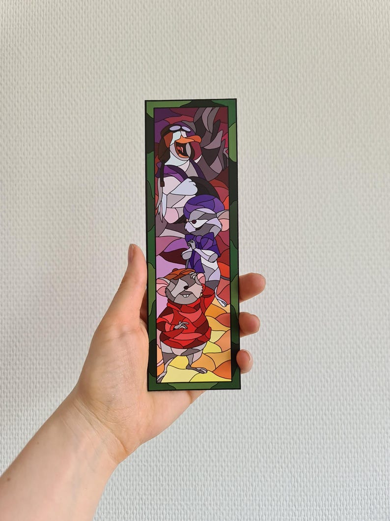 Op de afbeelding: Een glas-in-lood bladwijzer met personages uit de animatiefilm De Reddertjes. De bladwijzer toont een muis in een rode trui, een muis in een paarse sjaal en een pingu&iuml;n in een wit-zwarte hoed.