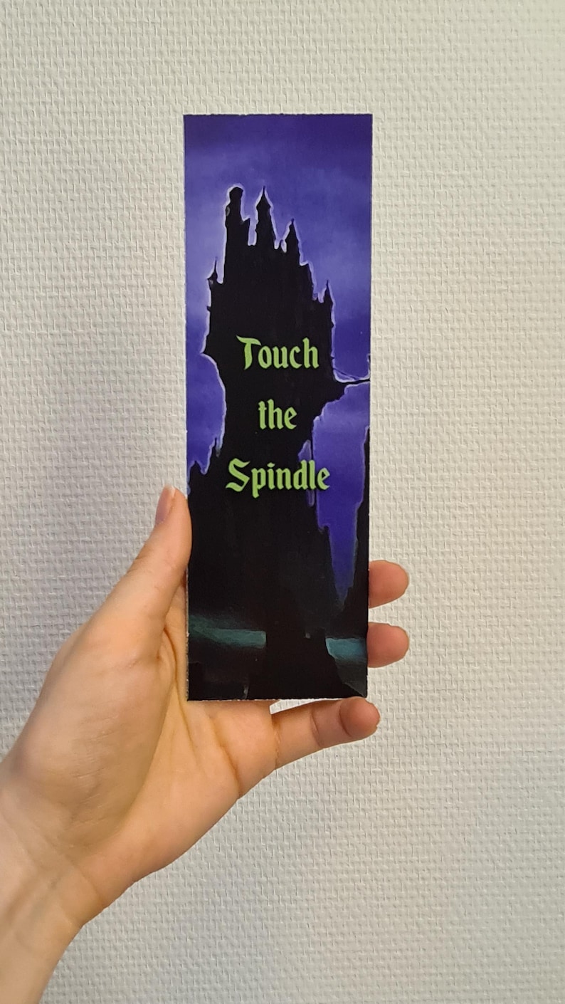 Puede incluir: Un marcap&aacute;ginas morado y negro con una silueta de un castillo y el texto "Touch the Spindle".