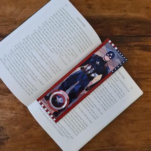 Può includere: Un segnalibro colorato di Captain America con un design a vetrata. Il segnalibro rettangolare, con bordo rosso, raffigura il personaggio in una posa dinamica, con il suo scudo in evidenza.