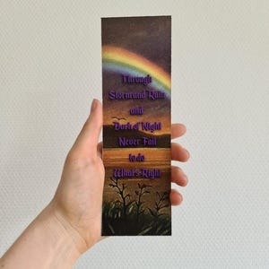 Op de afbeelding: Een bladwijzer met een zonsondergangsc&egrave;ne en een regenboog. De tekst op de bladwijzer luidt "Through Storm and Rain and Dark of Night Never Fail to do What's Right."