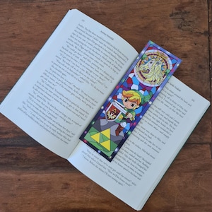 Op de afbeelding: Een gekleurd glas-bladwijzer met een personage uit de videogame-serie The Legend of Zelda. De bladwijzer is een levendige mix van blauw, groen, geel en rood. Het personage houdt een zwaard en schild vast, en de achtergrond heeft het Triforce-symbool.