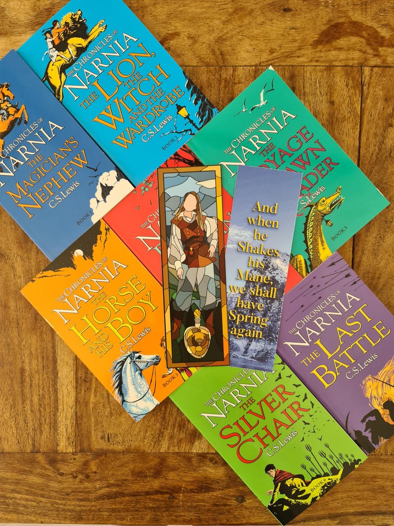 May include: A collection of ten books from the Chronicles of Narnia series by C.S. Lewis. The books are arranged in a semi-circle on a wooden surface. The books are all different colors and have illustrations on the covers.