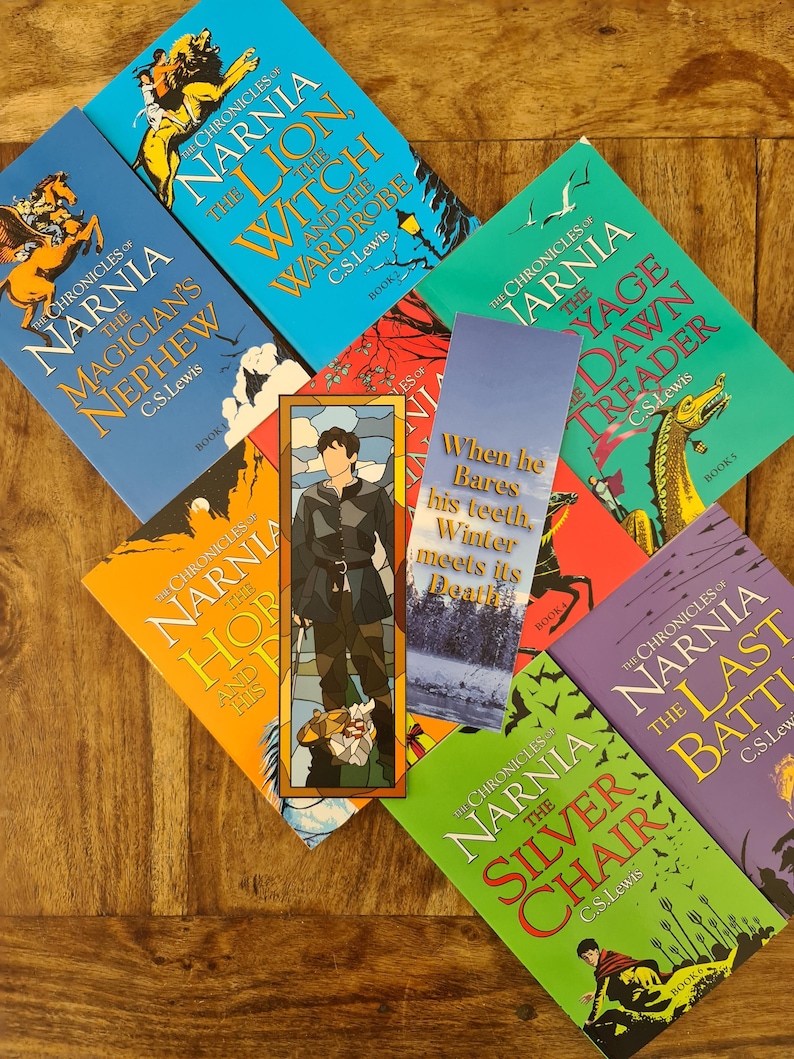 May include: A collection of seven paperback books from the Chronicles of Narnia series by C.S. Lewis. The books are arranged in a semi-circle on a wooden surface. The titles of the books are: The Magician's Nephew, The Lion, the Witch and the Wardrobe, The Horse and His Boy, The Voyage of the Dawn Treader, The Silver Chair, and The Last Battle.
