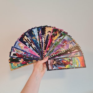 Op de afbeelding: Een verzameling kleurrijke glas-in-lood-bladwijzers met verschillende Disney-figuren. De bladwijzers zijn in een waaier gerangschikt en worden in een hand gehouden.