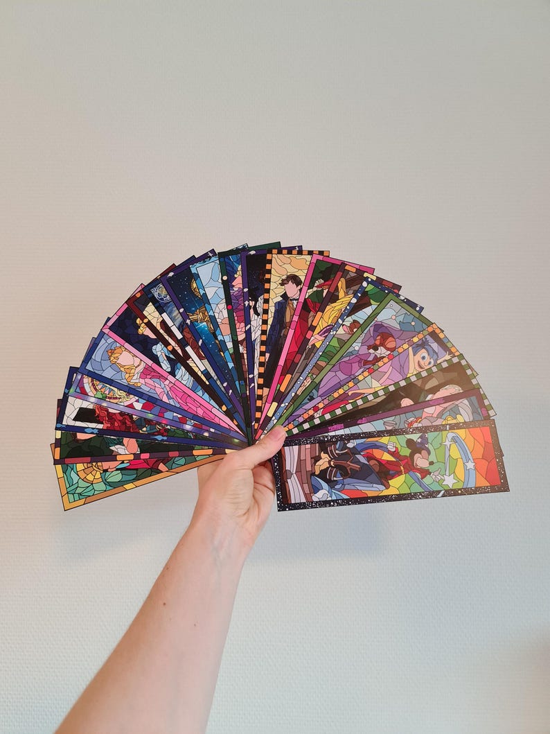 Op de afbeelding: Een verzameling kleurrijke glas-in-lood-bladwijzers met verschillende Disney-figuren. De bladwijzers zijn in een waaier gerangschikt en worden in een hand gehouden.