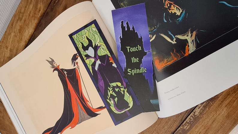 Puede incluir: Dos marcadores de p&aacute;gina con Mal&eacute;fica de la pel&iacute;cula de Disney La Bella Durmiente. Un marcador es un dise&ntilde;o de vitral con Mal&eacute;fica con un vestido morado y cuernos verdes. El otro marcador es una silueta negra del castillo de Mal&eacute;fica con el texto "Touch the Spindle".