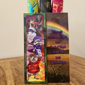 Op de afbeelding: Twee kleurrijke bladwijzers met illustraties in de stijl van glas-in-lood. De linker bladwijzer toont een cartoonmuis en een pingu&iuml;n. De rechter bladwijzer toont een regenboog en de tekst "Through Storm and Rain and Dark of Night Never Fail to do What's Right".