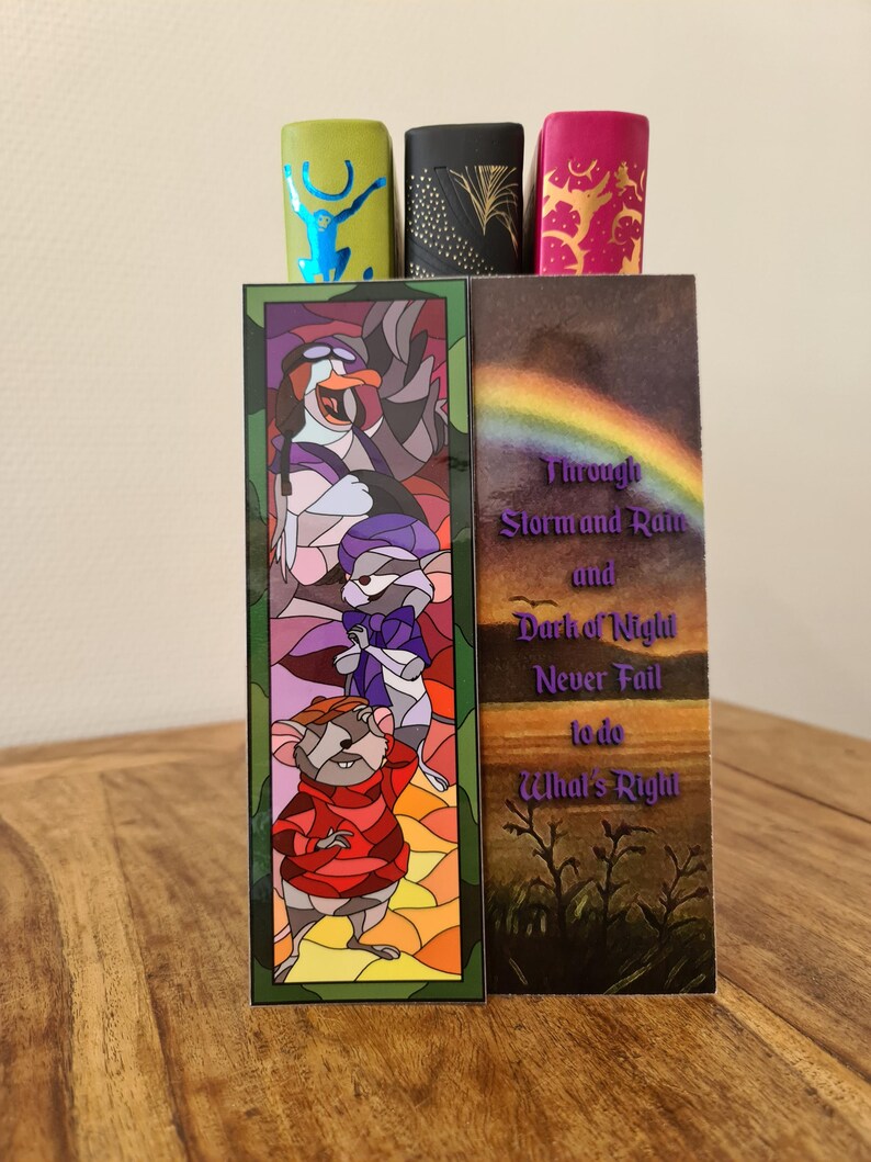 Op de afbeelding: Twee kleurrijke bladwijzers met illustraties in de stijl van glas-in-lood. De linker bladwijzer toont een cartoonmuis en een pingu&iuml;n. De rechter bladwijzer toont een regenboog en de tekst "Through Storm and Rain and Dark of Night Never Fail to do What's Right".