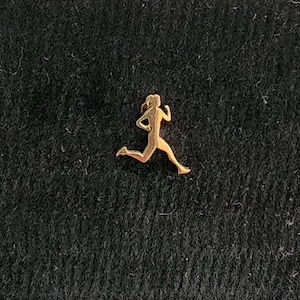 Puede incluir: Un amuleto de metal dorado en forma de persona corriendo.