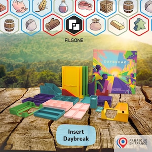 Pode incluir: Um jogo de tabuleiro chamado "Daybreak" com várias inserções de jogo coloridas. As inserções são em tons de verde, rosa, amarelo e roxo. A arte da caixa apresenta uma ilustração colorida de pessoas em uma estrada. O texto "Insert Daybreak" também é visível.