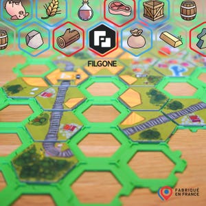 Könnte beinhalten: Ein Brettspiel mit grünen sechseckigen Kacheln und illustrierten Ressourcensymbolen. Das Spielbrett zeigt eine Landschaft mit Straßen und Gebäuden. Das Logo des Spiels, "FILGONE", ist sichtbar, zusammen mit dem Text "FABRIQUÉ EN FRANCE."