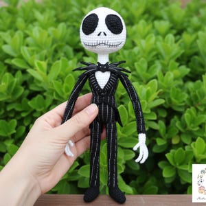 Peut inclure: Poupée Jack Skellington au crochet. La poupée a une tête blanche avec des yeux noirs et une bouche cousue. Elle porte un costume noir à fines rayures blanches, un nœud papillon en forme de chauve-souris et des gants blancs. La poupée mesure environ 30 cm de haut.
