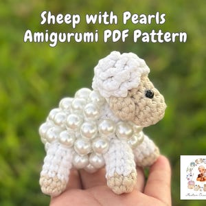 May include: White crocheted amigurumi sheep with pearl beads, a PDF pattern for crocheting the sheep is included. The sheep is sitting on a hand.