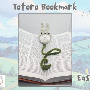 Puede incluir: Un marcapáginas de ganchillo con un personaje de Totoro gris, con una panza blanca y una cola verde en forma de vid, colocado en un libro abierto. El texto "Totoro Bookmark" está en la parte superior y "Easy" en la inferior derecha.