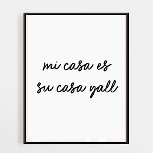 Puede incluir: Un estampado enmarcado con el texto "mi casa es su casa yall" en escritura cursiva negra sobre un fondo blanco. El marco es de color marrón oscuro. La obra de arte es una pieza decorativa.